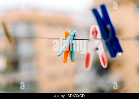 Bright clothespins hang on a wire, supporting children’s clothes that are drying after rain. The scene shows droplets on the pins and a blurred city b Stock Photo