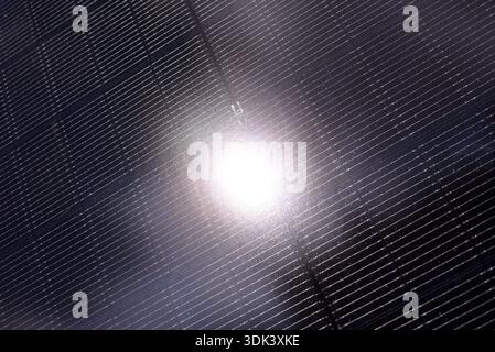 Close view of a solar panel surface showing numerous photovoltaic cells. The sunlight reflects off the surface, creating a bright spot. The shot captu Stock Photo