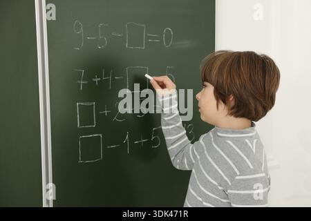 Schoolboy doing math on chalkboard in classroom Stock Photo