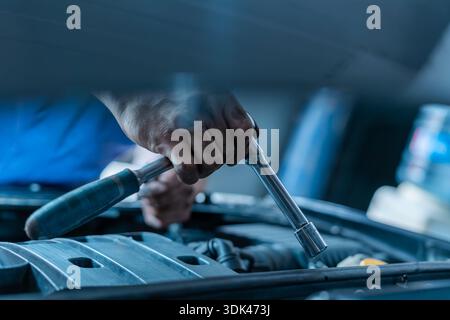 Hand holding a socket  wrench over a car engine Stock Photo