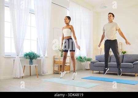 Smiling couple doing cardio jumps at home, staying active, healthy in living room Stock Photo
