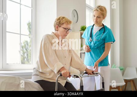 Senior woman and caregiver in medical room, young nurse assisting older patient sitting on bed Stock Photo