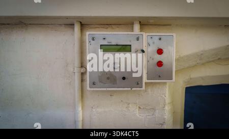 Wall-mounted security intercom control panel with small lcd screen and red buttons on a white brick wall in an industrial hallway. Stock Photo