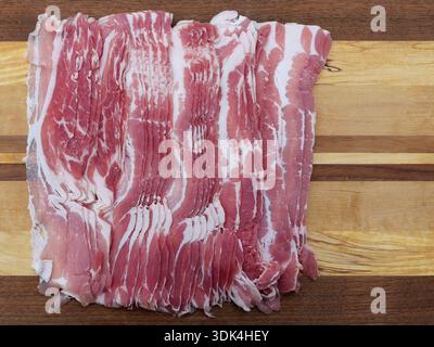 Thinly sliced smoked pork belly arranged on rustic wooden cutting board ...