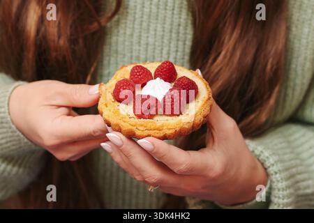 Raspberry tartlet held in hands closeup. Fresh fruit dessert with cream filling. Homemade pastry served for sweet moment. Stock Photo