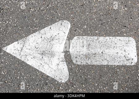 White directional arrow painted on asphalt road surface. Traffic guidance symbol and urban transportation marking outdoors closeup. Stock Photo