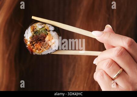 Sushi roll with baked salmon held by chopsticks closeup. Japanese cuisine detail. Fresh rice seaweed and fish. Homemade sushi preparation concept. Stock Photo