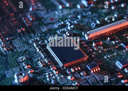 A dramatic close-up of a microchip on a printed circuit board, illuminated with red and blue light, showing dense circuitry, soldered pins, and advanc Stock Photo