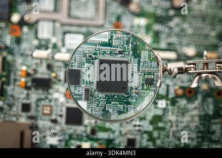A magnifying glass focuses on a microchip mounted on a circuit board, revealing fine electronic traces and components, symbolizing inspection, precisi Stock Photo