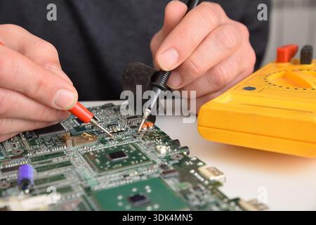 Close-up of an electronic technician testing a circuit board with a multimeter during hardware Stock Photo
