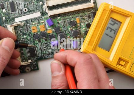 Close-up of an electronic technician testing a circuit board with a multimeter during hardware. Top view. Stock Photo