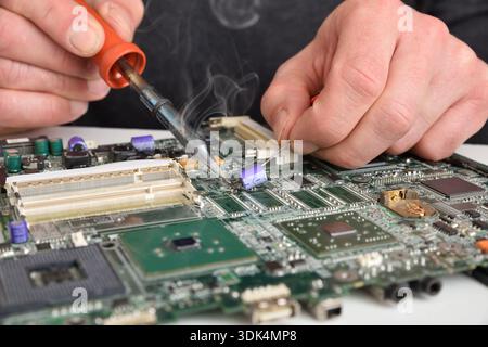 Close-up of an electronics technician soldering components on a motherboard during professional circuit board repair and hardware maintenance. Front v Stock Photo