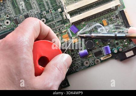 Technician soldering electronic components on a circuit board using a soldering iron during professional PCB repair and microelectronics maintenance. Stock Photo