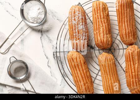 Grid with tasty eclairs, sieves and sugar powder on marble background Stock Photo