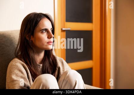 Young woman sitting, thinking, lost in thought Stock Photo