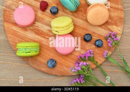 Board with sweet macaroons and berries on wooden background Stock Photo