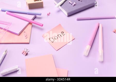 Sticky note with word DONE and stationery on lilac background Stock Photo