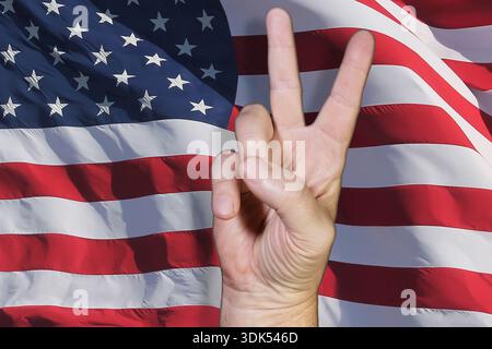 Man's hand showing the peace or victory sign in front of the US flag Stock Photo