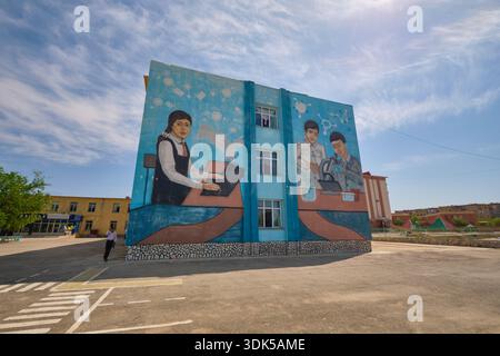 A large, colorful mural on the side of a school. Kids using a laptop, studying science. In Uchkuduk, Uzbekistan. Stock Photo