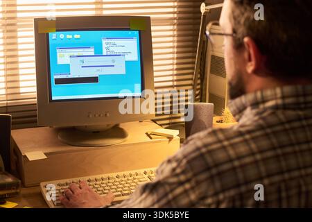Middle aged Caucasian man using desktop computer with CRT monitor, installing software or updating system, sitting at desk in office environment, hands on keyboard and mouse Stock Photo