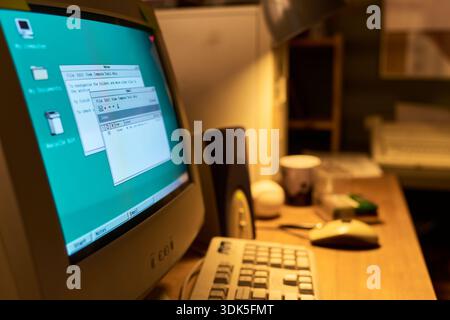 Old CRT computer monitor displaying classic graphical user interface with open text editor windows, keyboard and mouse on wooden desk in retro office workspace Stock Photo