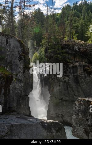 A glimpse of Nairn Falls as the Green River funnels through a rocky canyon beneath forested cliffs on a bright day in British Columbia. Stock Photo