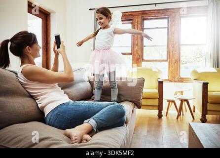 Recording, girl and mom with smartphone, online and child with costume for ballet rehearsal in home. Happy, woman and bonding with kid, memory and Stock Photo