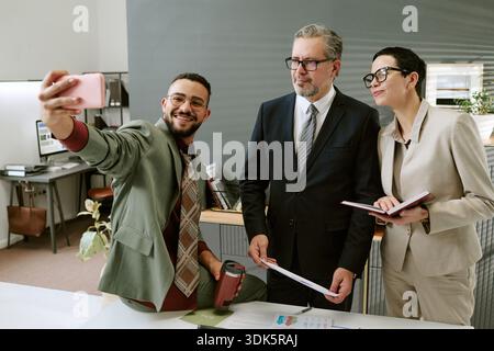 Young Adult Man Taking Selfie with Middle Aged Colleagues Stock Photo