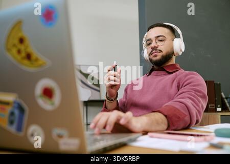 Young Adult Man Wearing Headphones Working on Laptop at Desk Stock Photo