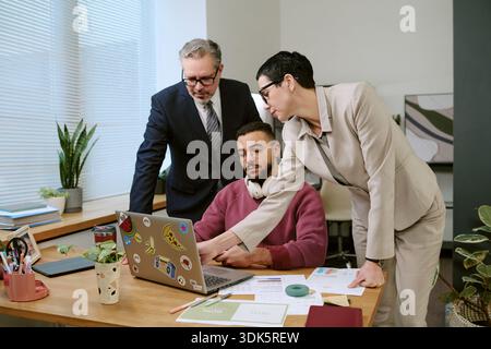 Middle Aged Man and Woman Guiding Young Adult Man Using Laptop Stock Photo