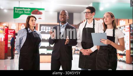 Successful Entrepreneur Guides Multiracial Supermarket Staff Toward Business Growth Together. Stock Photo