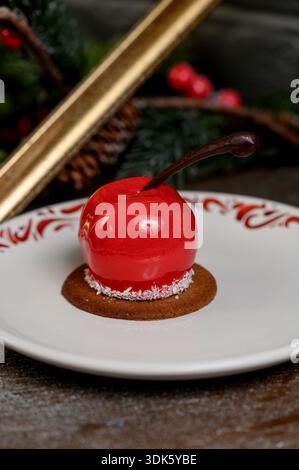Red apple shaped cake with glossy icing on a white plate.A bright red mousse cake on a plate in a cozy New Year's interior with pine needles Stock Photo