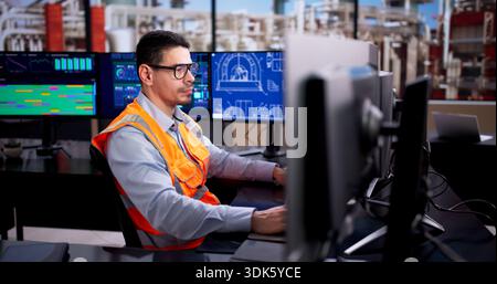 Young Latino Industrial Engineer Monitors Automated System On Desktop Screen. Stock Photo