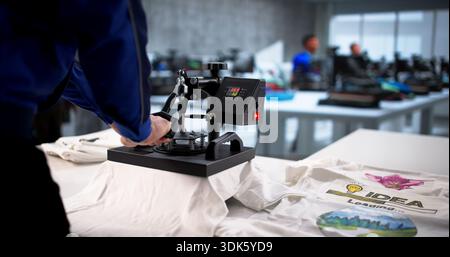Young Latino Employee Creating Custom T-shirt Designs With Heat Press Stock Photo