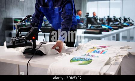 Young Hispanic Man Printing Custom T-shirts Using Heat Press Machine. Stock Photo