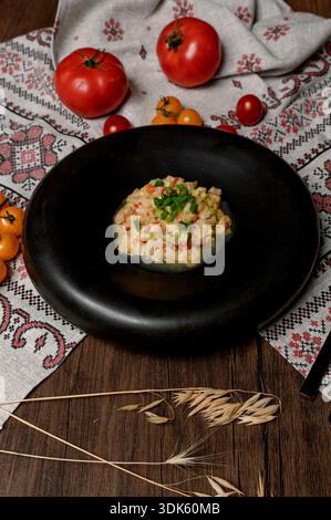 Vegetable tartare with green onions in a black deep plate. Appetizer of finely chopped vegetables in a black ceramic bowl on a wooden table Stock Photo