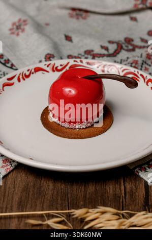 Red apple shaped cake with glossy icing on a white plate.A bright red mousse cake on a plate in a cozy interior Stock Photo