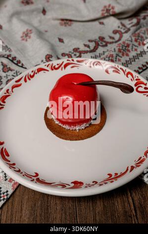Red apple shaped cake with glossy icing on a white plate.A bright red mousse cake on a plate in a cozy interior Stock Photo
