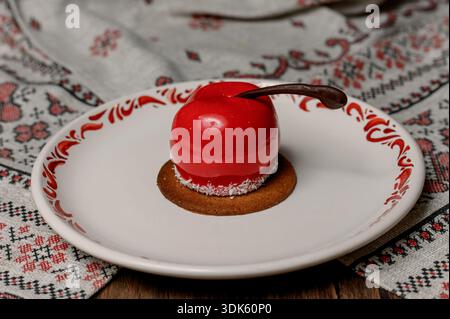 Red apple shaped cake with glossy icing on a white plate.A bright red mousse cake on a plate in a cozy interior Stock Photo
