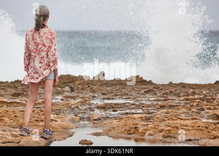 Senior woman looking the sea. Waves breaking on the shore Stock Photo