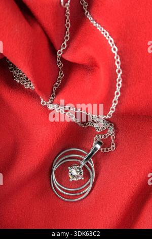 White gold necklace lying on red draped silk fabric background Stock Photo