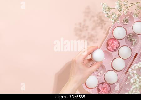 Easter Composition with Female Hand Placing White Easter Eggs Into Pink Tray Adorned With Spring Flowers And Gypsophila To Represent Elegant Easter Ho Stock Photo