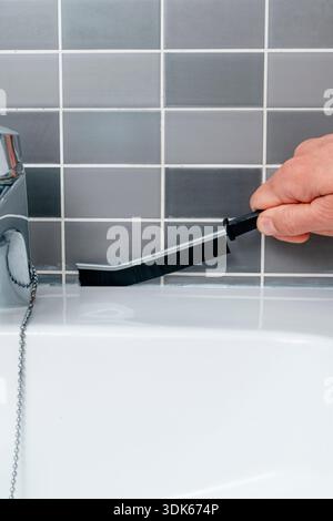 a close view of a man using a special brush to scrub the joints along the bathroom sink, removing dirt from the tiled surface Stock Photo