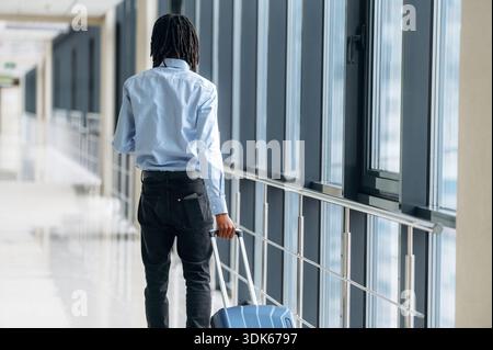 Walking with suitcase. Male tourist is in the airport corridor. Stock Photo