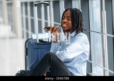 Sitting on the floor with phone in hand. Male tourist is in the airport corridor. Stock Photo