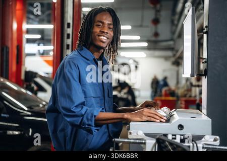 Stationary computer with display. Male mechanic is with car in garage. Stock Photo