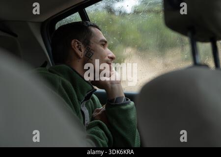Man with face tattoo looking through rainy car window Stock Photo