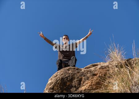 Man making victory peace signs sitting on rock Stock Photo