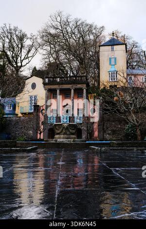 Colorful Fountain and Anchor houses with pink and yellow facades frame a central fountain courtyard in Portmeirion village, their vibrant reflections Stock Photo