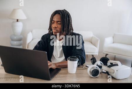 Using computer. Young man is sitting by table with laptop and virtual reality glasses. Stock Photo